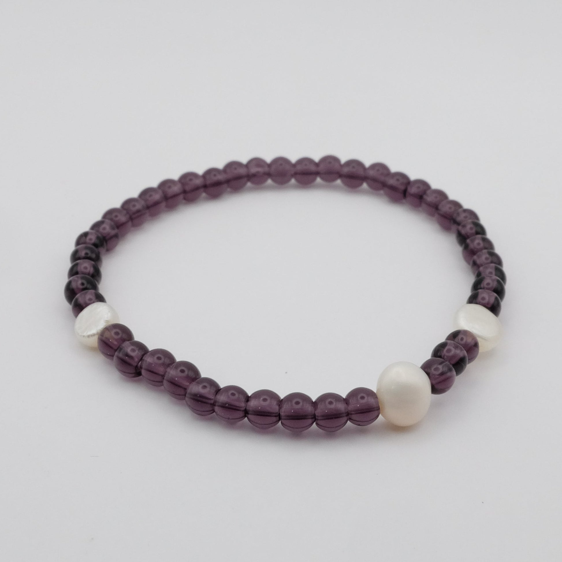 Beaded bracelet with purple and white beads on a light gray background