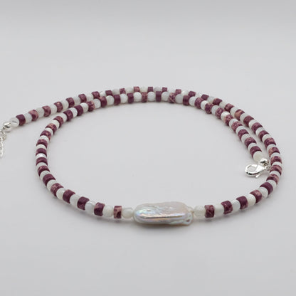 A handmade beaded necklace featuring purple sea sediment jasper heishi gemstone beads, mother of pearl beads and a baroque freshwater pearl focal bead, displayed on a white background.