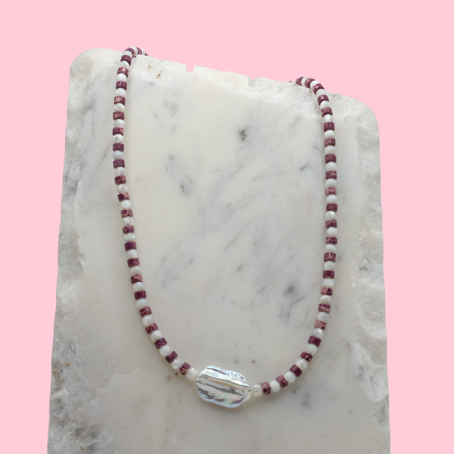 Necklace with red and white beads on a marble surface with a pink background