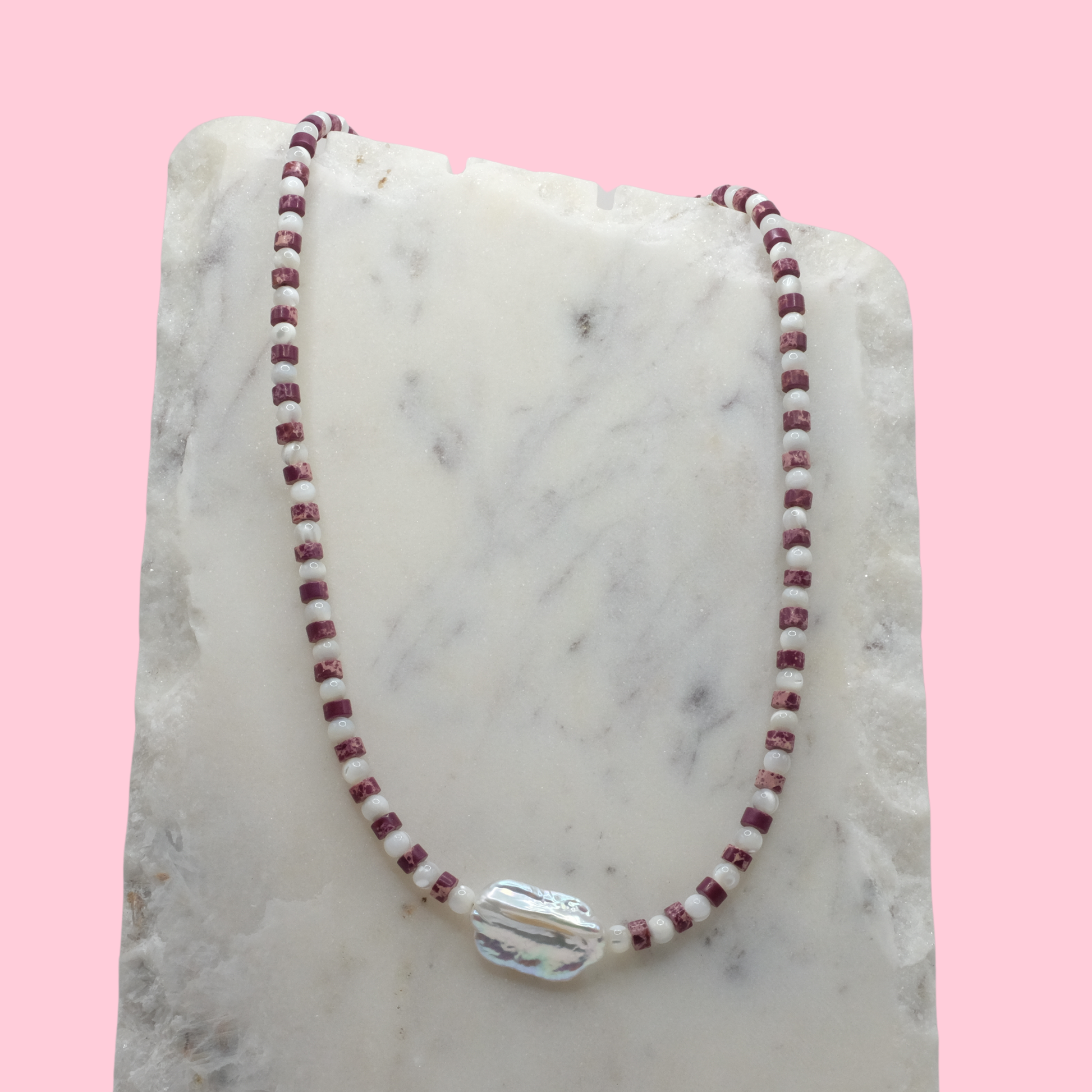 Necklace with red and white beads on a marble surface with a pink background