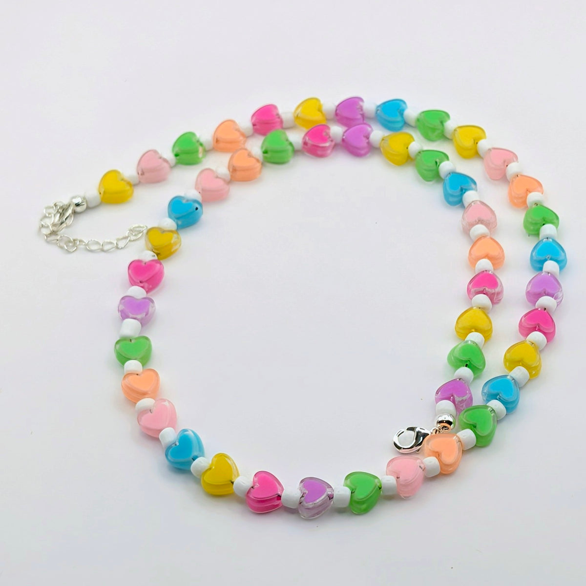 Colourful handmade beaded necklace featuring rainbow translucent heart beads, white glass seed beads and silver-plated findings with an extension chain.