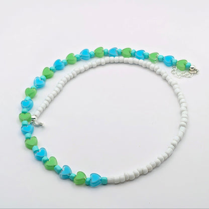 A beaded necklace featuring alternating strands of white round beads, light blue heart-shaped beads, and lime green heart-shaped beads, displayed on a clean white background.
