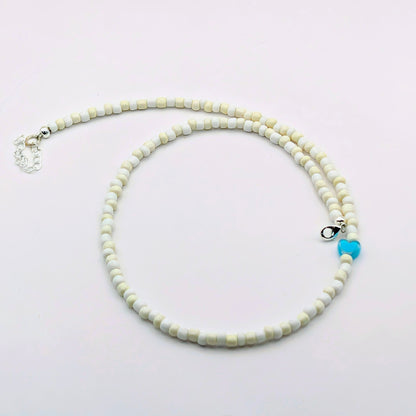 A handmade beaded necklace with cream and white glass beads, bright blue heart feature bead and silver clasp and extension chain.