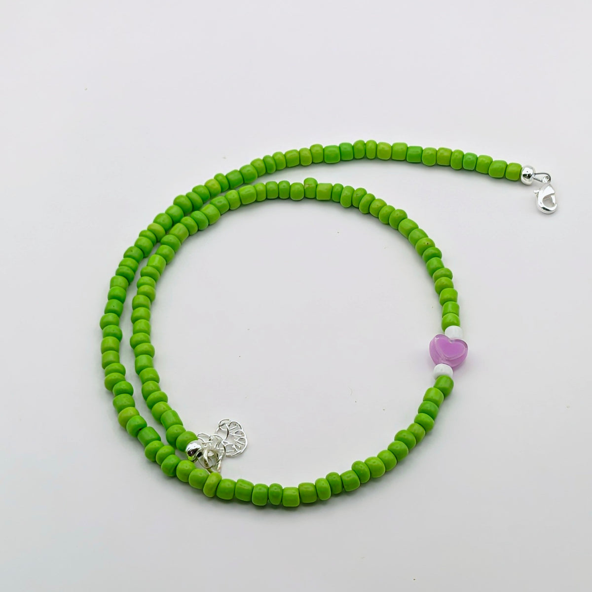 A handmade beaded necklace with bright green glass beads, white accents, purple heart feature bead and silver clasp.