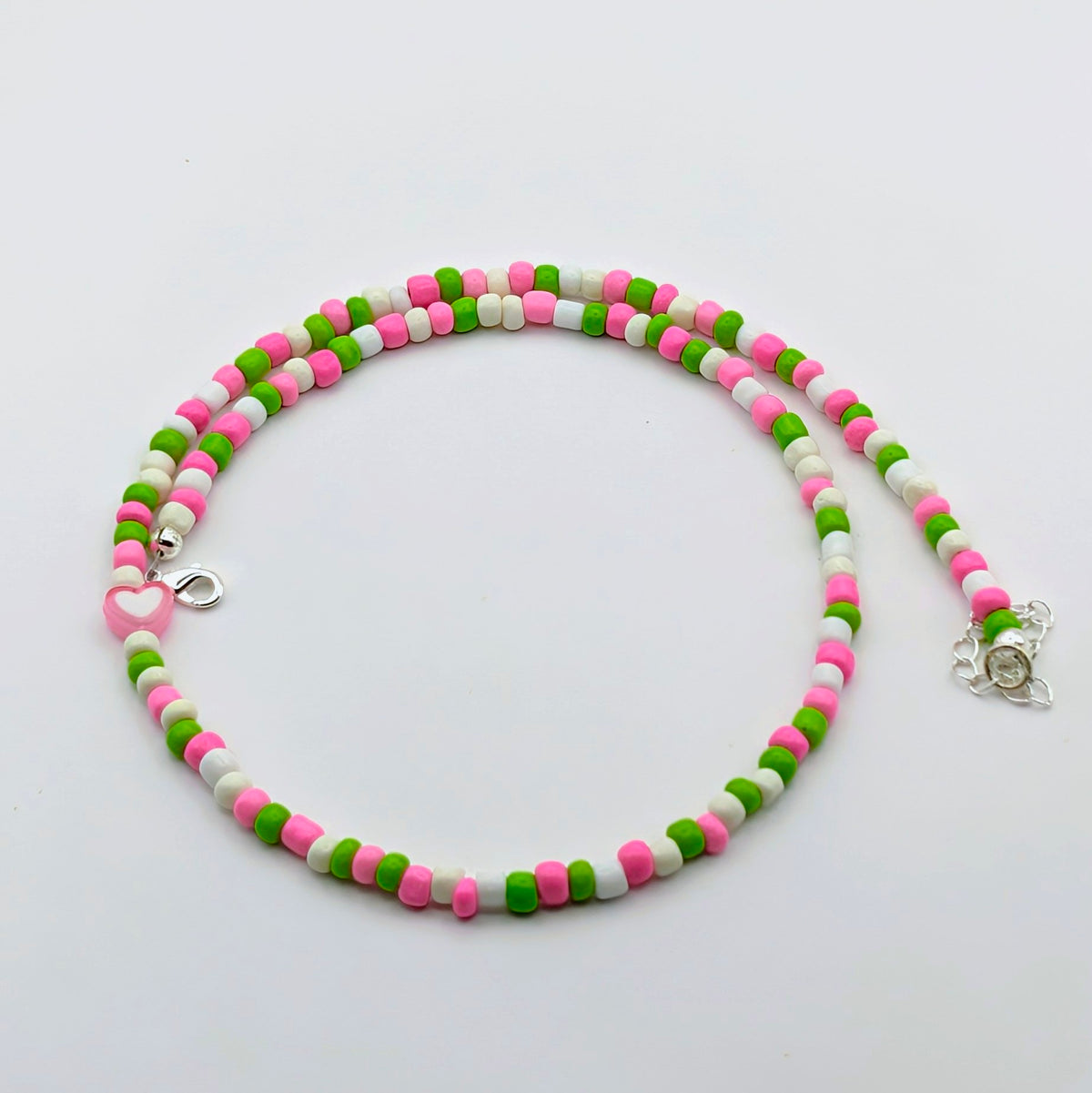 Acolourful handmade beaded necklace with pink, green and white glass beads, pink heart feature bead and silver hardware.
