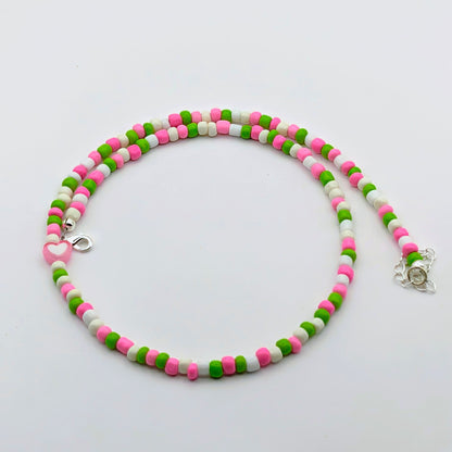 Acolourful handmade beaded necklace with pink, green and white glass beads, pink heart feature bead and silver hardware.