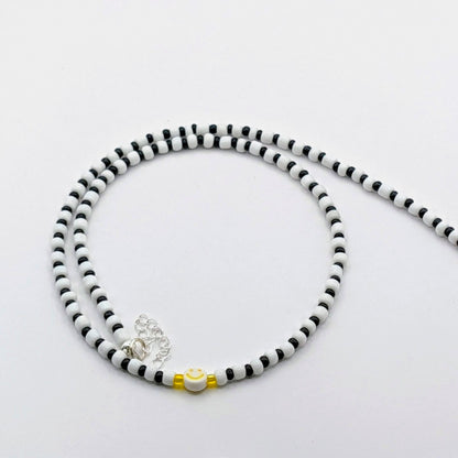 Black and white Phoebe handmade beaded necklace with glass beads and a yellow smiley bead, quirky statement jewellery.