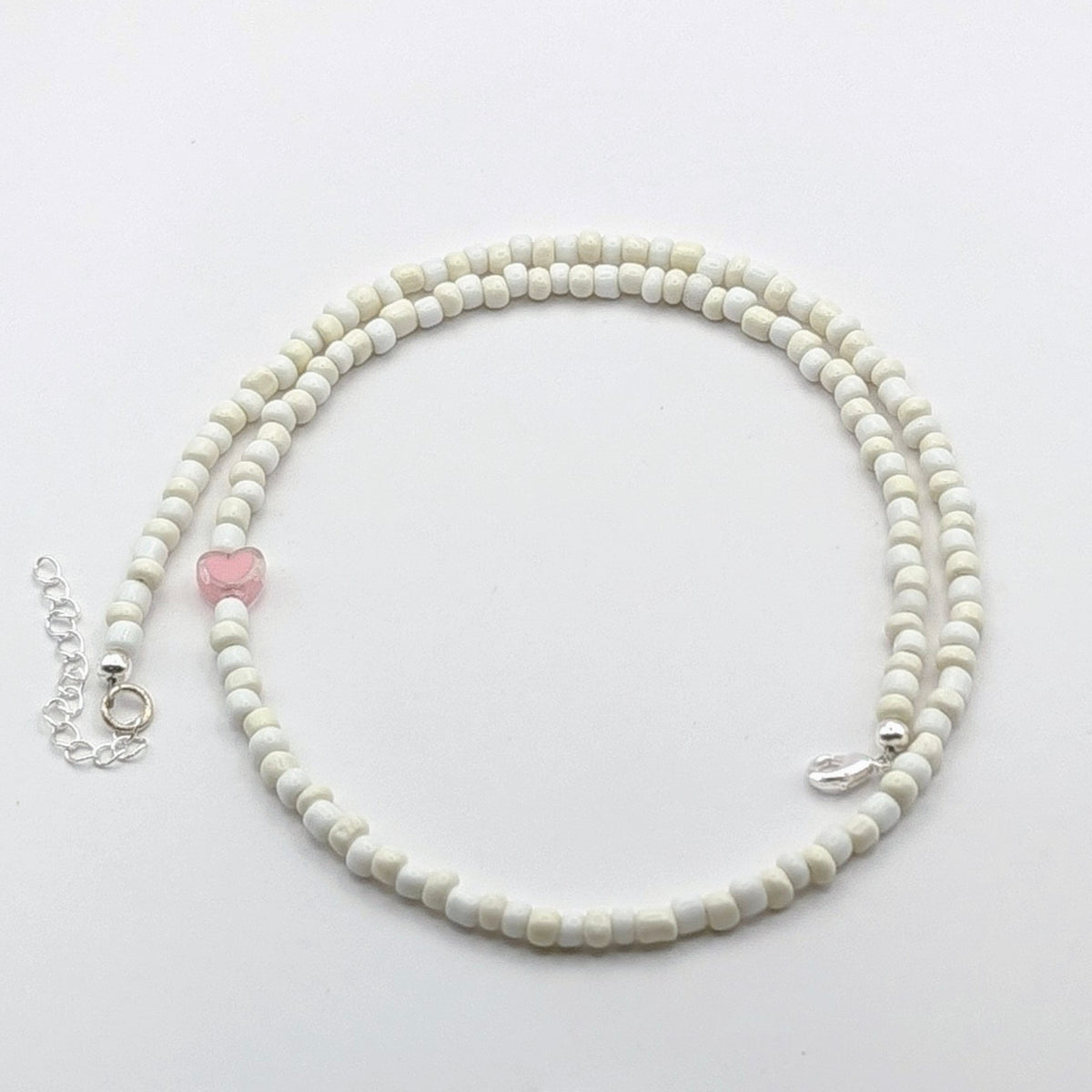 A handmade beaded necklace with cream and white glass beads, translucent pink heart feature bead and silver hardware.