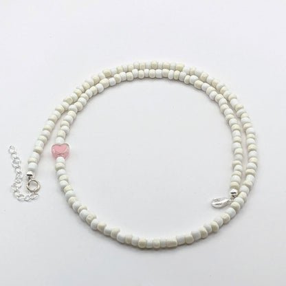 A handmade beaded necklace with cream and white glass beads, translucent pink heart feature bead and silver hardware.