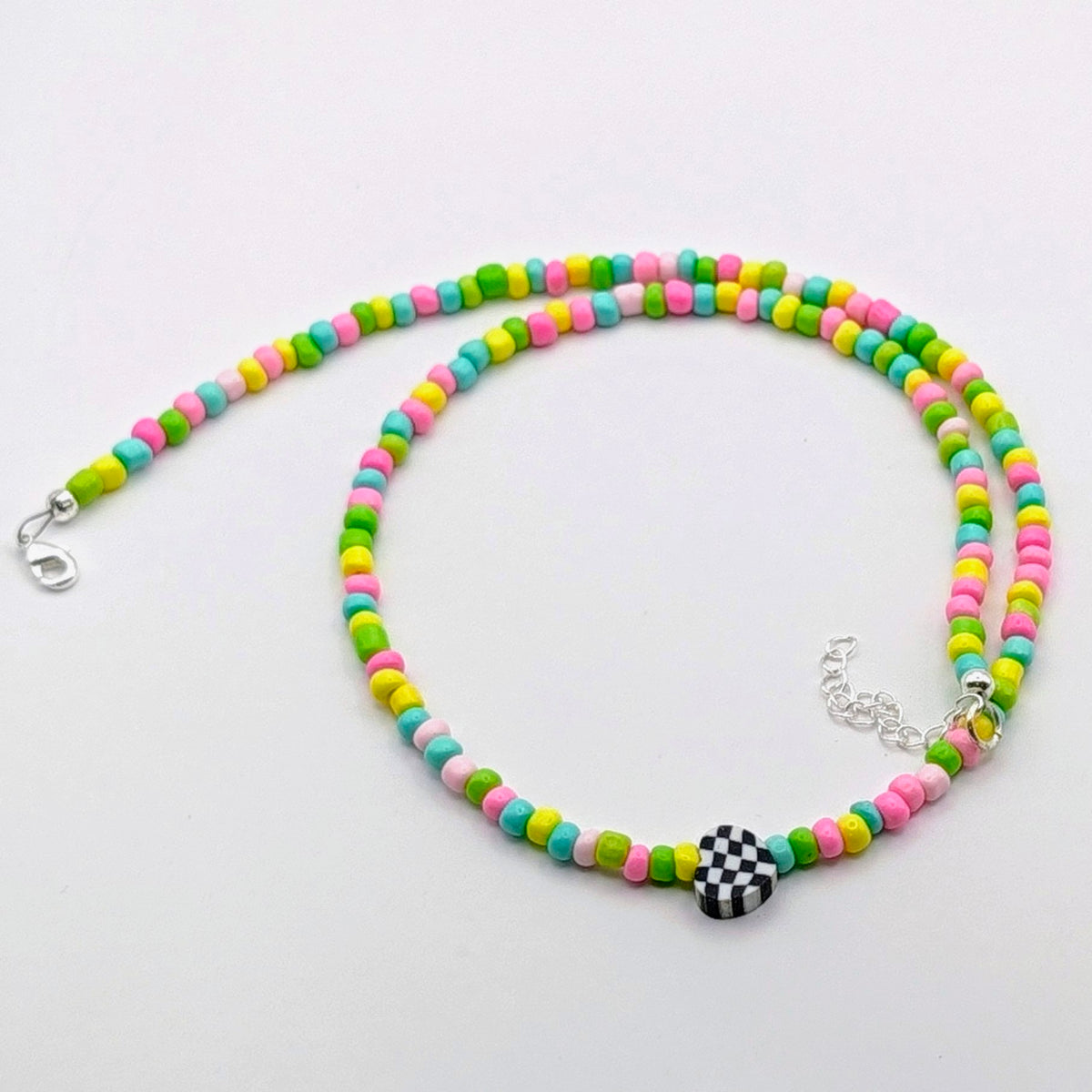 A colourful handmade beaded necklace with pink, green, blue and yellow glass beads and a black and white checkerboard heart centrepiece.