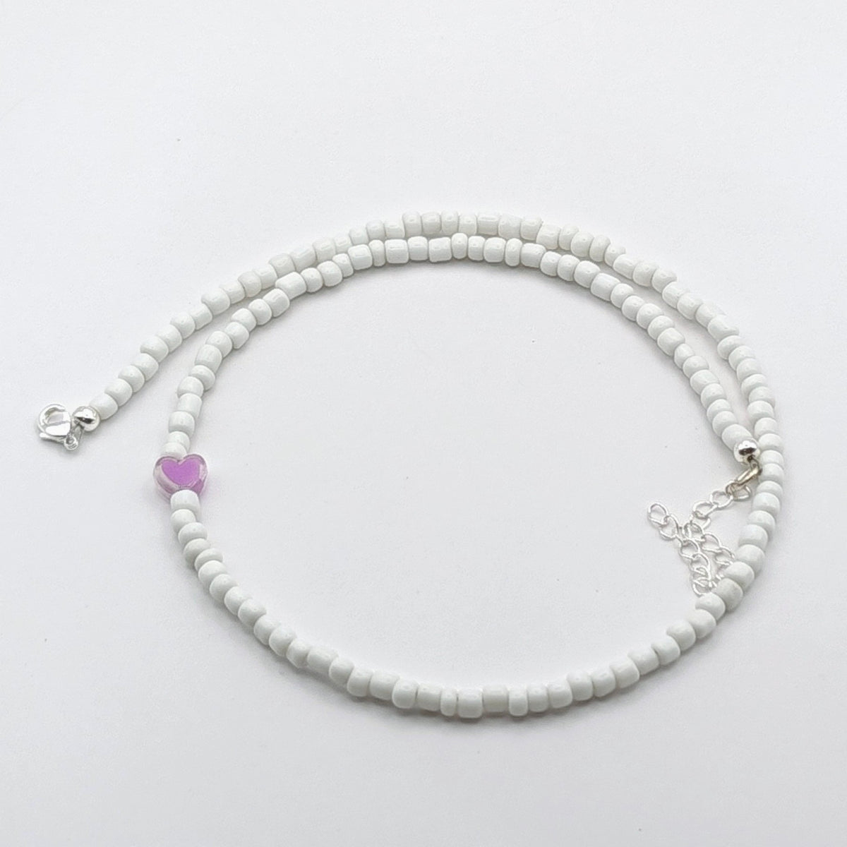 A handmade beaded necklace with white glass beads, purple heart feature bead and silver clasp and extension chain.