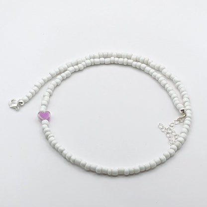 A handmade beaded necklace with white glass beads, purple heart feature bead and silver clasp and extension chain.
