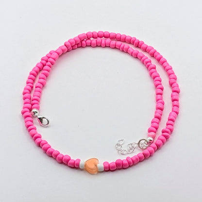 Sara handmade pink beaded necklace featuring bright pink glass beads, peach heart bead, white accents and silver hardware.