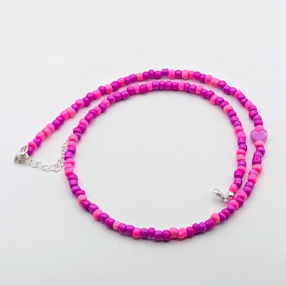 A colourful handmade beaded necklace with bright pink and purple glass beads, purple heart feature bead and silver hardware