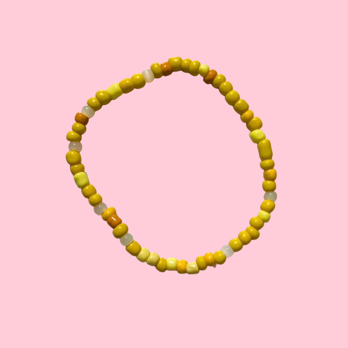 A beaded stretch bracelet made of small yellow and orange beads, displayed on a textured white wall.