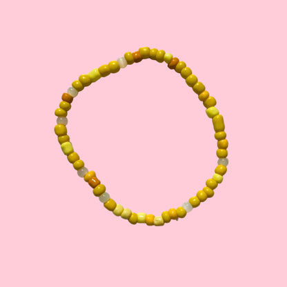 A beaded stretch bracelet made of small yellow and orange beads, displayed on a textured white wall.