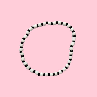 A circular black and white beaded necklace or bracelet displayed against a textured white wall.
