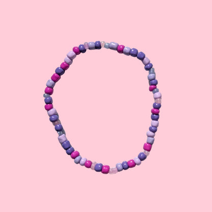 A beaded stretch bracelet made of small purple round beads, displayed on a textured white background.