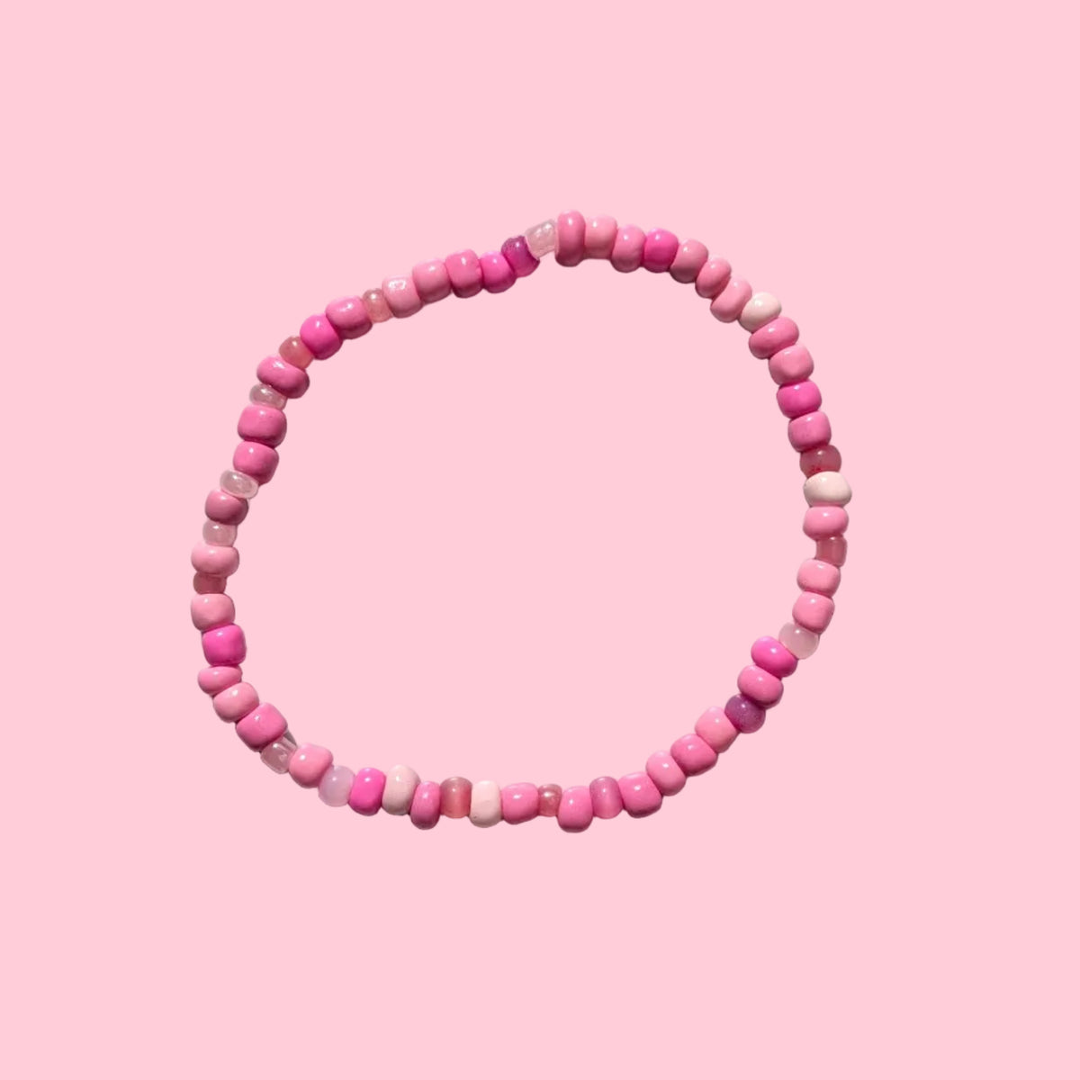 A beaded stretch bracelet made of small pink round beads, displayed on a textured white background.