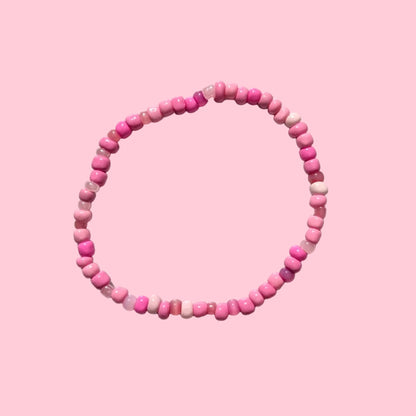 A beaded stretch bracelet made of small pink round beads, displayed on a textured white background.