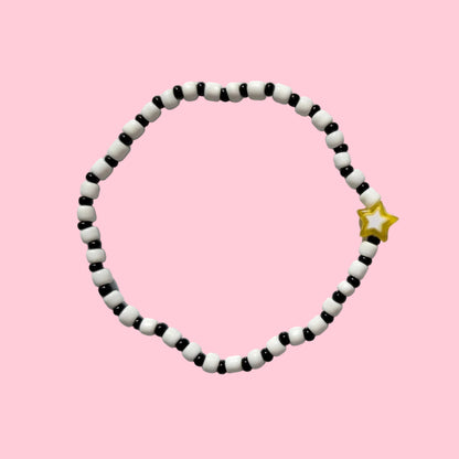 A beaded bracelet made of alternating black and white beads, featuring a small yellow star charm on one side, displayed against a textured white wall.