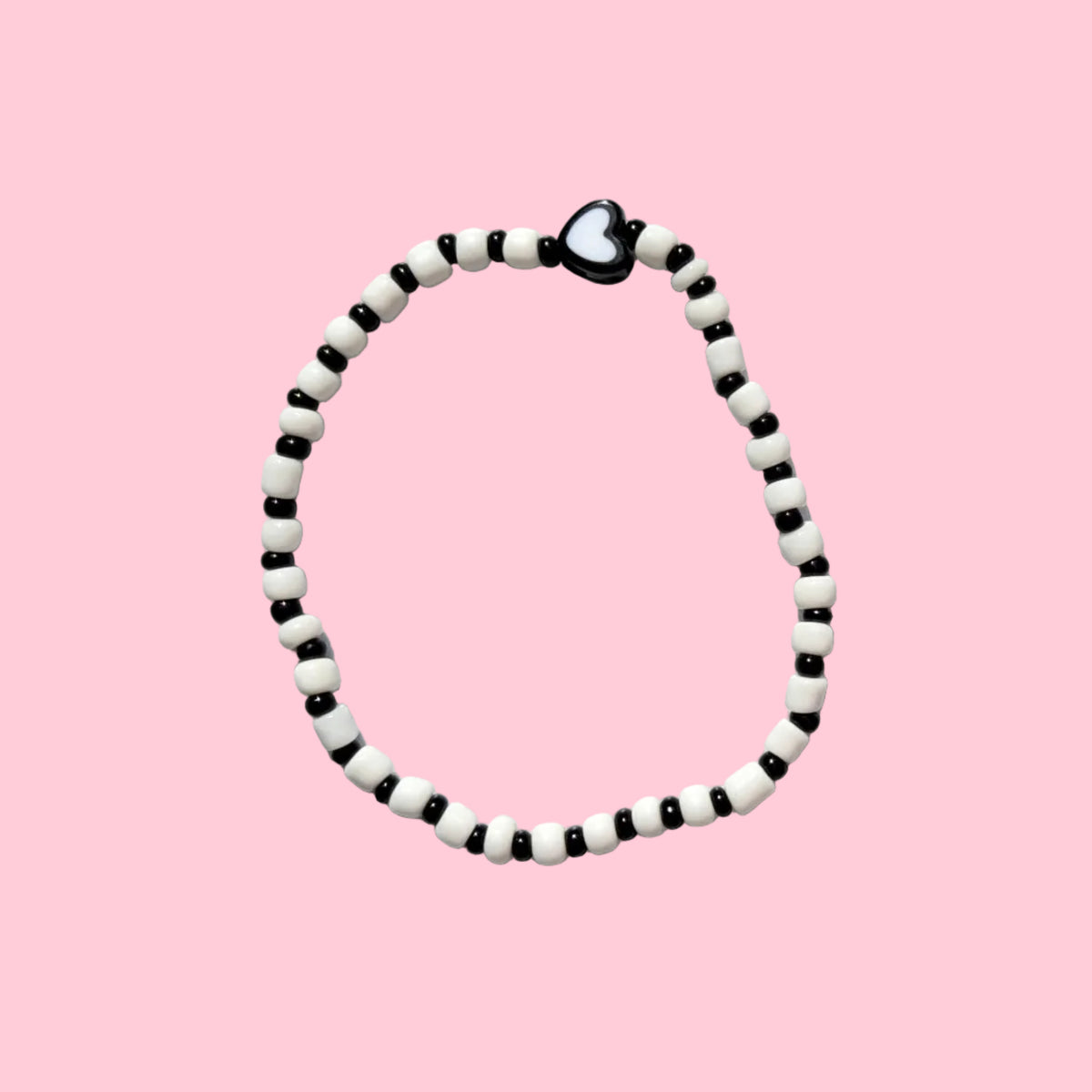 A beaded necklace with alternating black and white beads, featuring a small black heart charm at the top, displayed against a textured white wall.