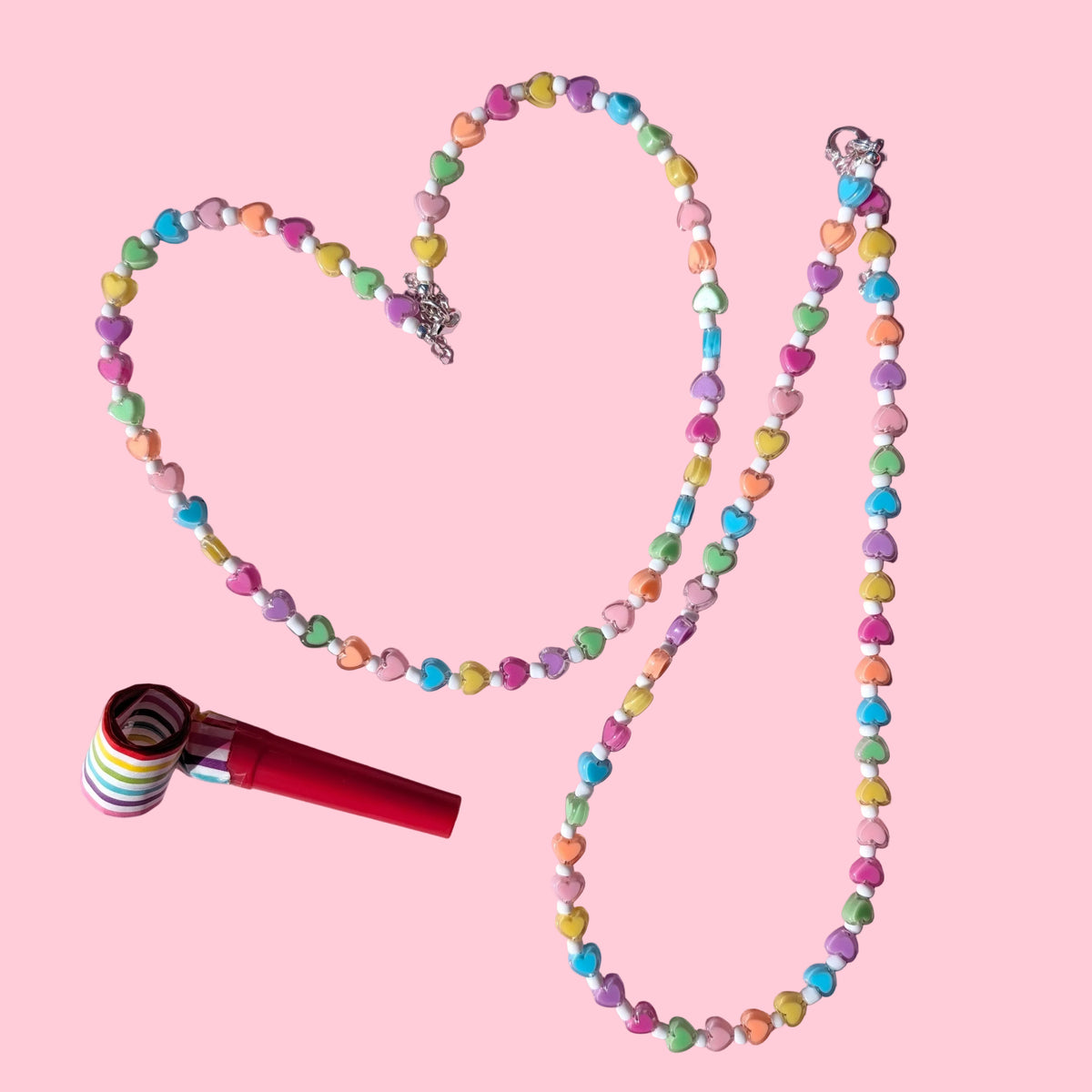 A beaded necklace made of pastel candy-coated beads arranged in a heart shape on a pink background, with a red and white striped lollipop-style charm placed beside it.