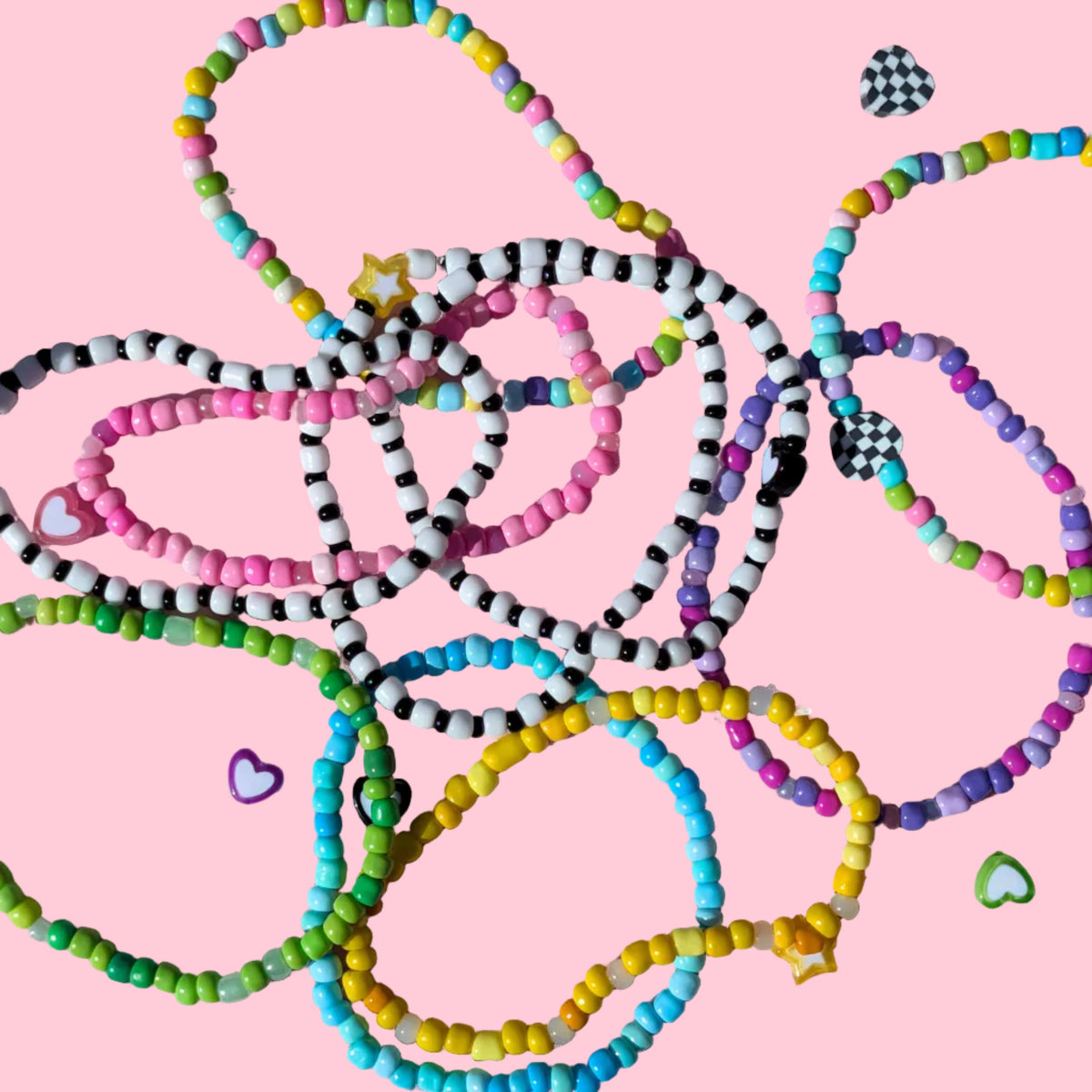 A pile of colorful beaded heart necklaces and bracelets arranged on a pink background with small heart-shaped accessories scattered around.