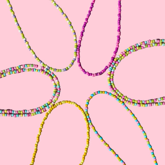 A group ofbbeaded flower-like necklaces in pink, yellow, and rainbow colors arranged on a light pink background.