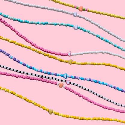 Several strands of small round beads arranged diagonally on a light pink fabric background. The beads come in multiple colorways, including pink, yellow, blue, white, black, and striped patterns.