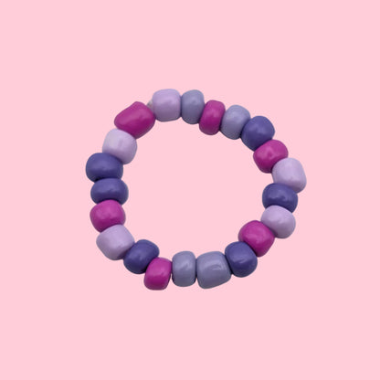 A beaded stretch ring made of small, faceted beads in alternating shades of purple, violet, and magenta, displayed on a clean white background.