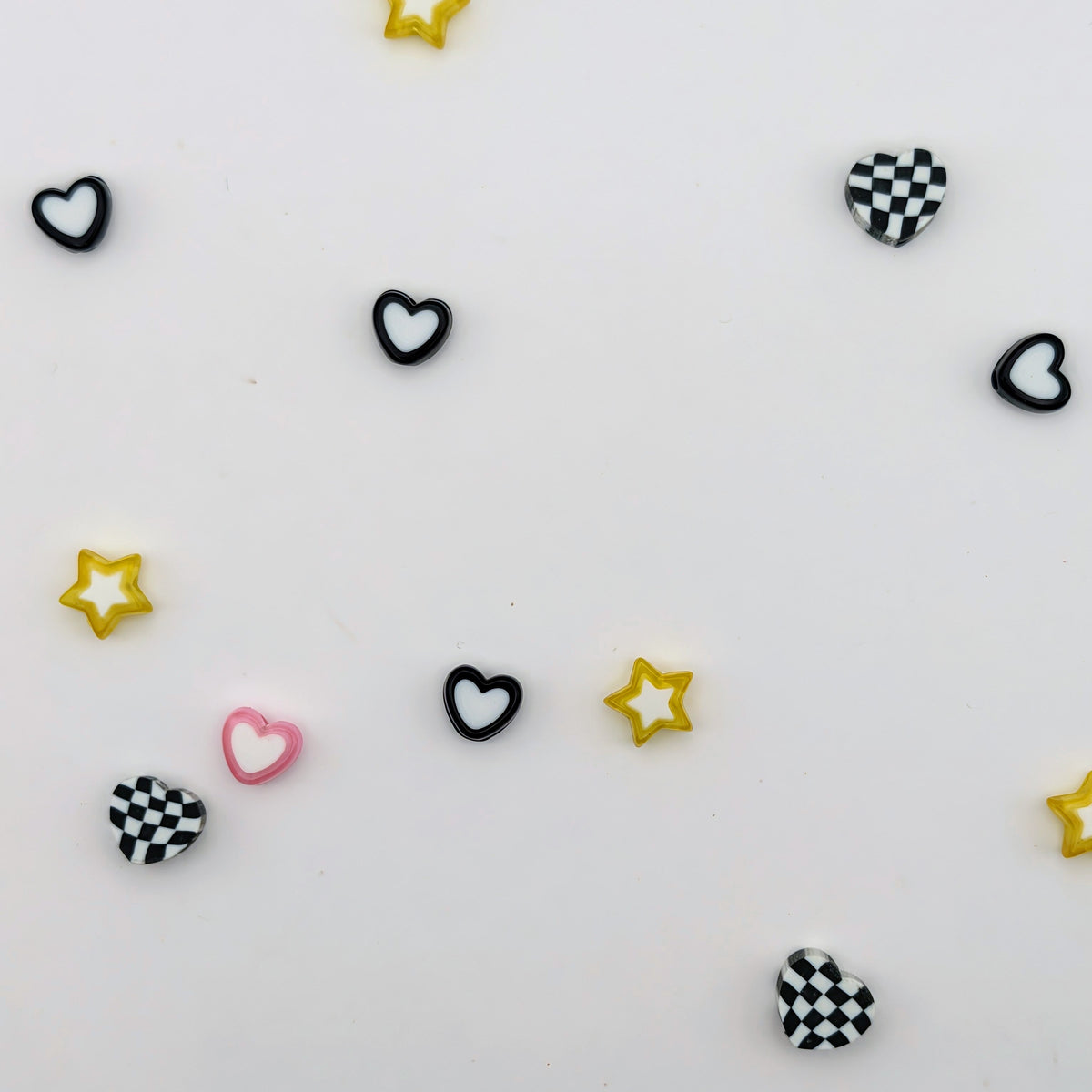 Small heart and star-shaped embellishments scattered on a white background, including solid black and pink hearts, black-and-white checkered hearts, and yellow outlined stars.