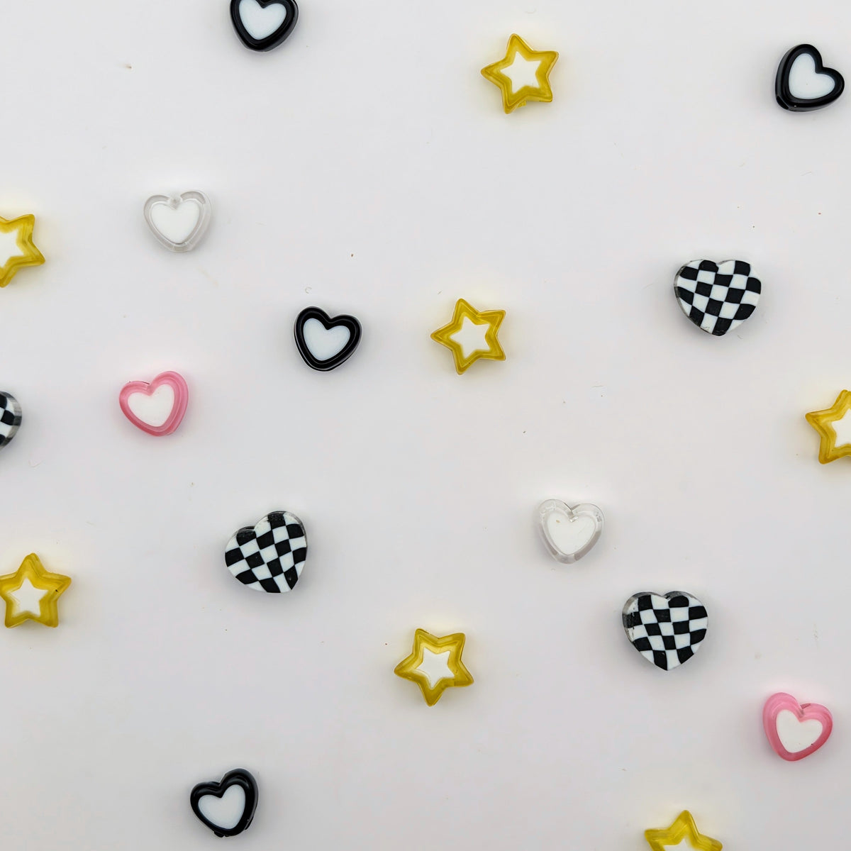 Small decorative heart and star embellishments scattered on a white background, including solid black, white, and pink hearts, black-and-white checkered hearts, and yellow star shapes.