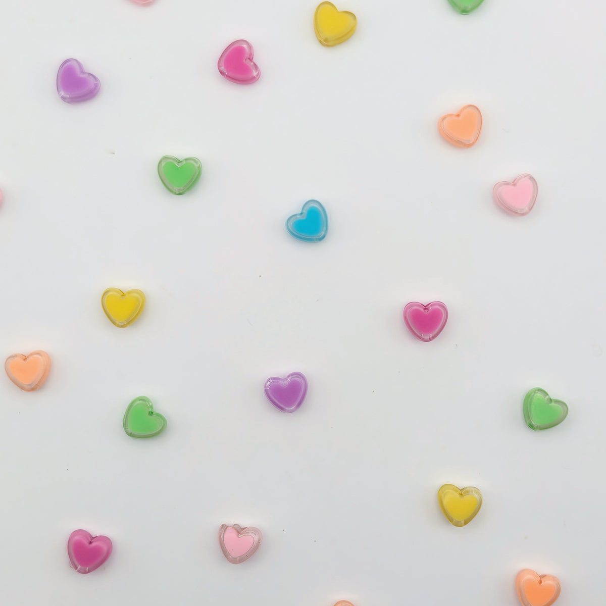Small translucent heart-shaped beads in pastel colors including pink, purple, green, yellow, orange, and blue scattered on a plain white background.