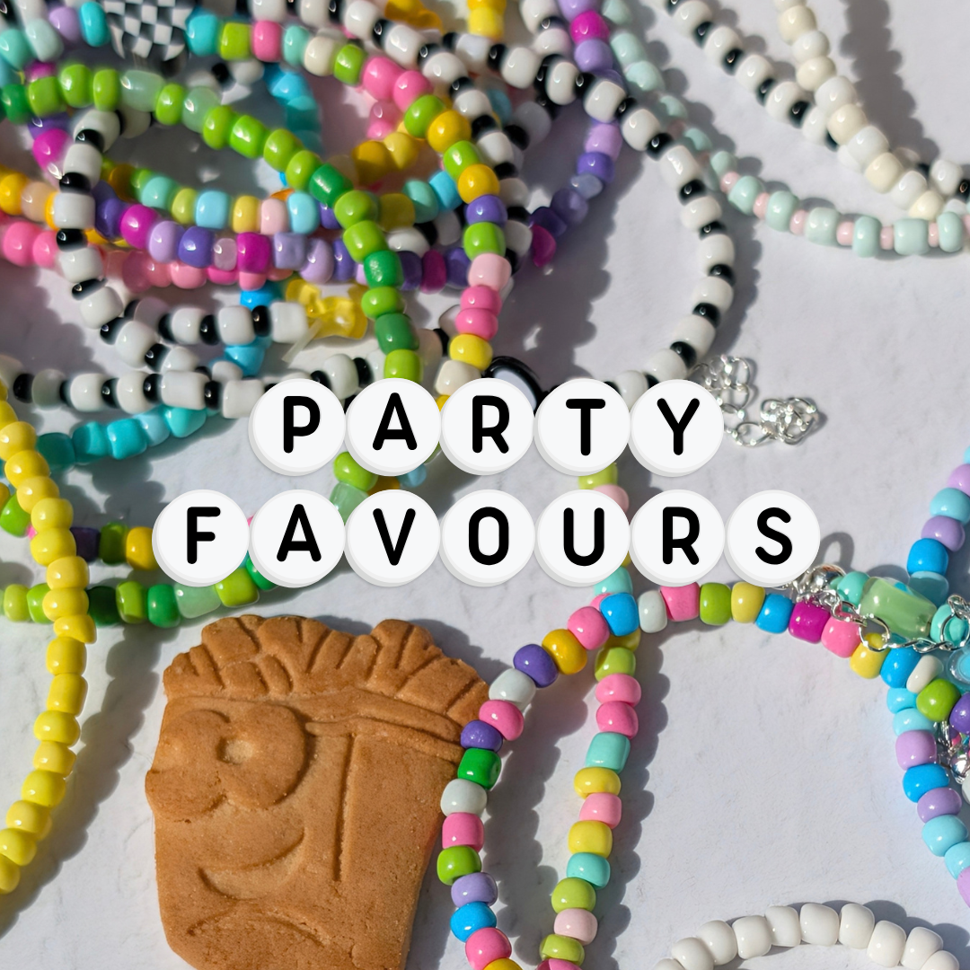 A collection of colorful party favors, including beaded necklaces and bracelets in various vibrant colors, a brown tiki-style charm, and white letter tiles spelling 'PARTY FAVOURS' in the center, all arranged on a white surface.