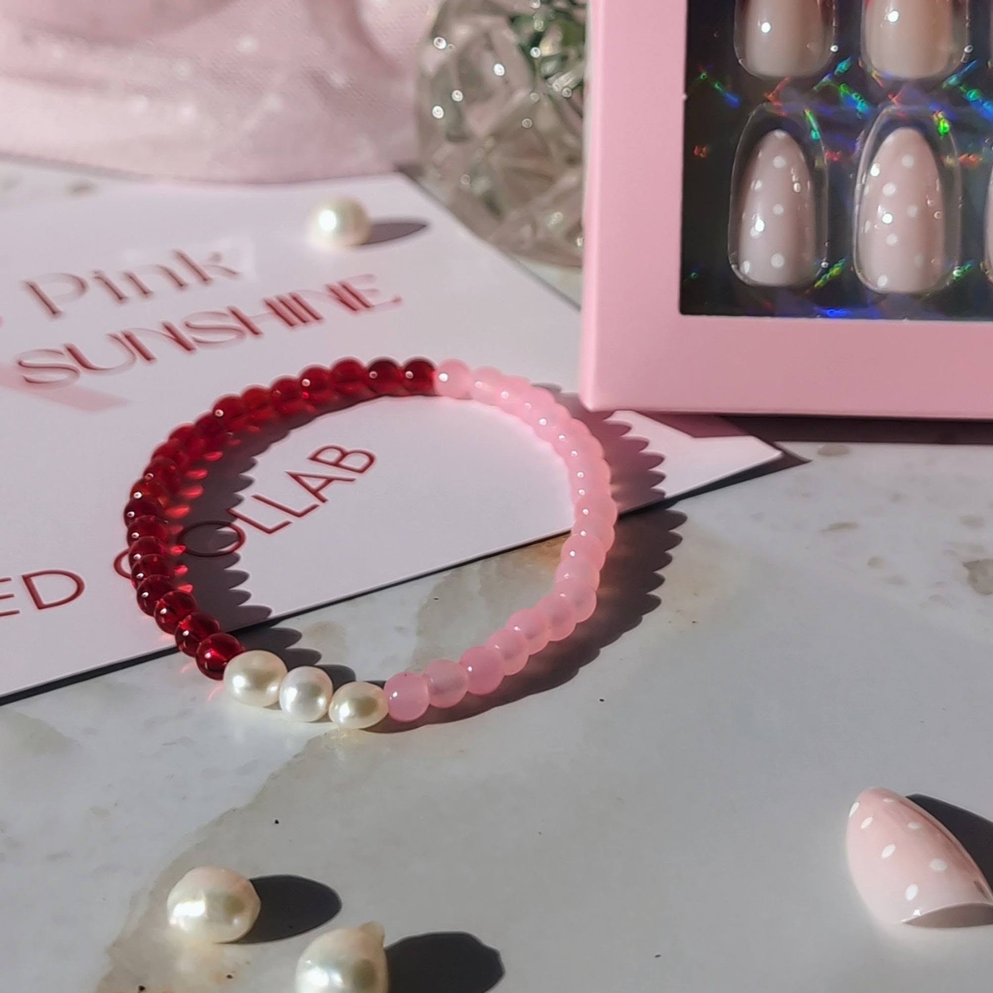 Pink hairband with pearls, nail display box, and red flowers on a light surface.