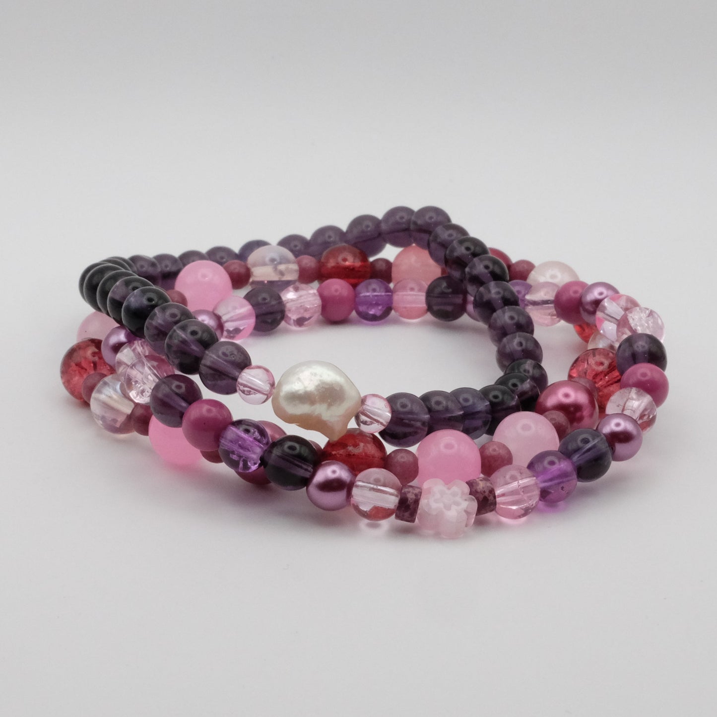 Set of three beaded bracelets with pink, purple, and red colors on a light gray background