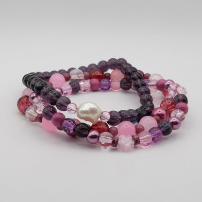 Set of three beaded bracelets with pink, purple, and red colors on a light gray background