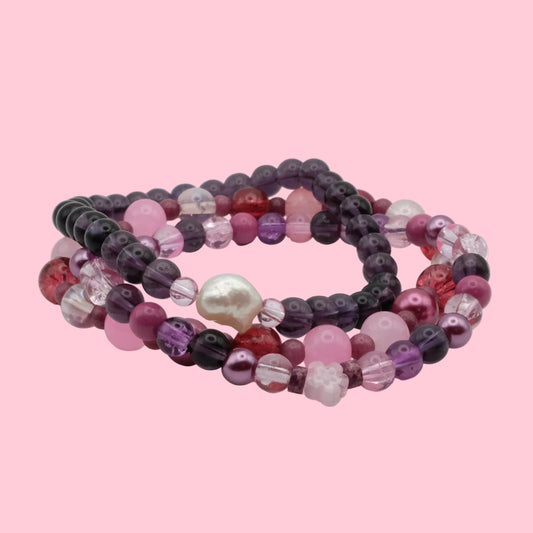 One-of-a-kind bracelet stack featuring pink, purple and berry-toned glass beads, floral accents and crystal details.