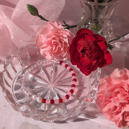 Clear crystal dish with red and pink flowers and a bracelet on a pink fabric background