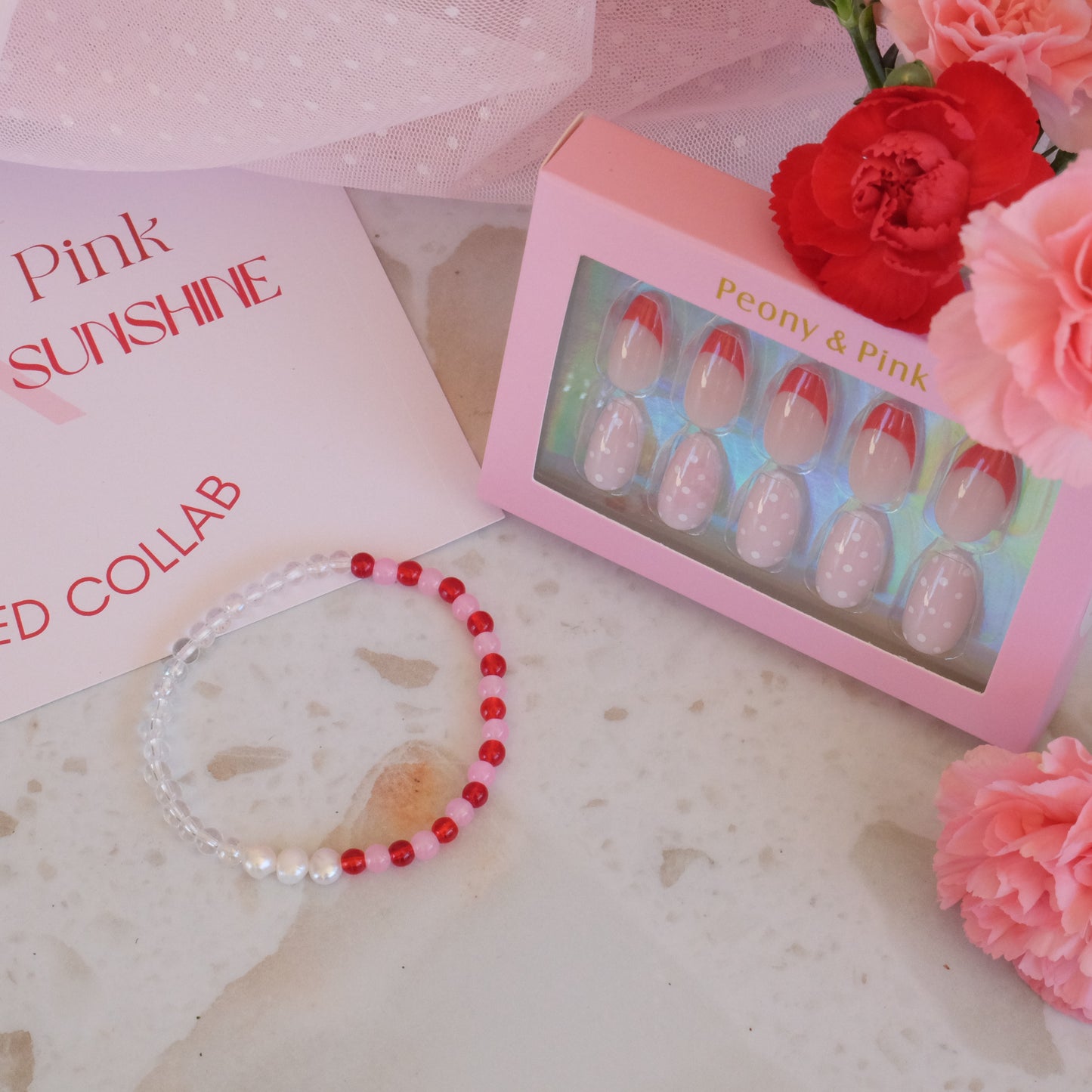 Bracelet with red and white beads, nail art set, and flowers on a textured surface.