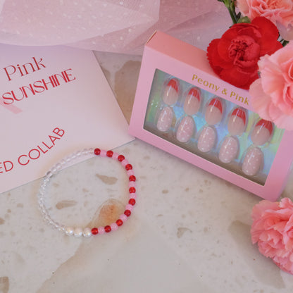 Bracelet with red and white beads, nail art set, and flowers on a textured surface.