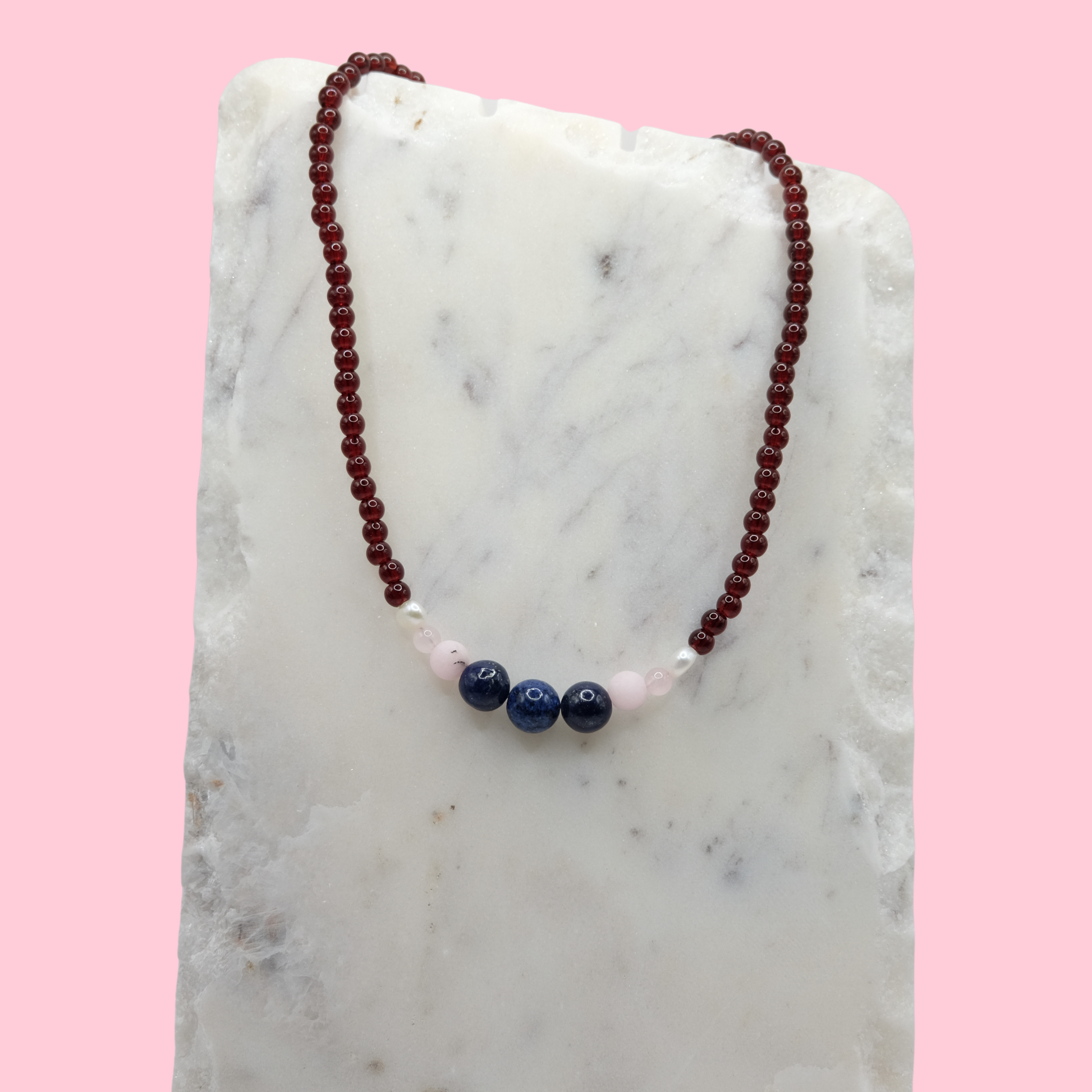 Necklace with red, pink, and blue beads on a marble surface with a pink background