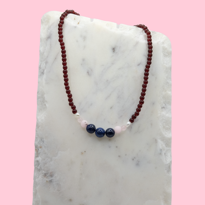 Necklace with red, pink, and blue beads on a marble surface with a pink background