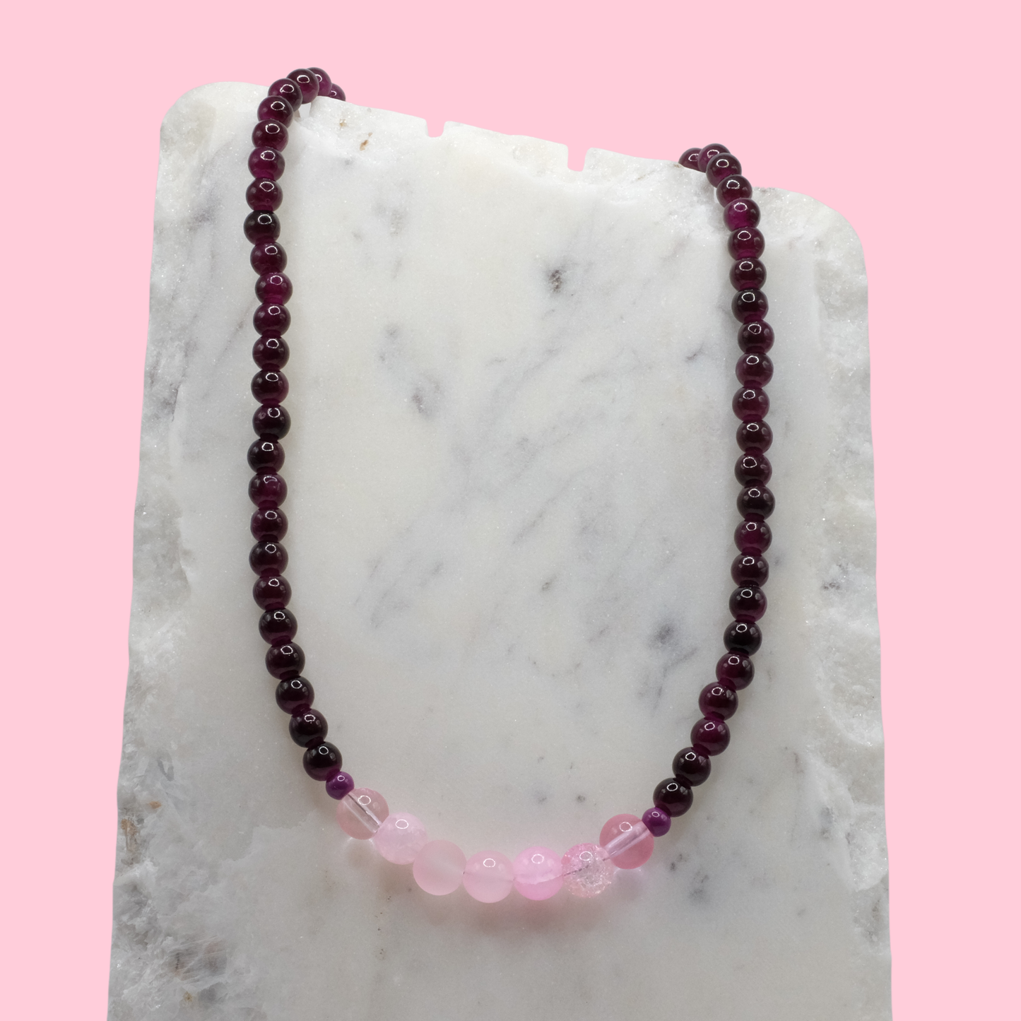 Beaded necklace with purple and pink beads on a marble surface with a pink background