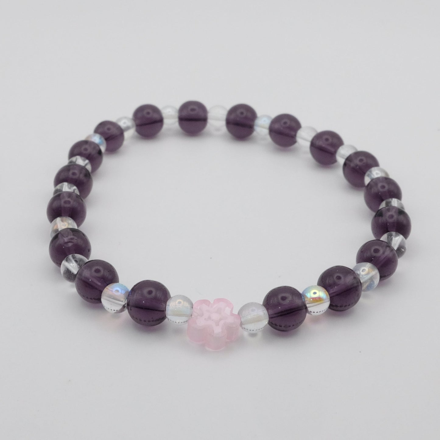Purple beaded bracelet with a pink heart charm on a light gray background