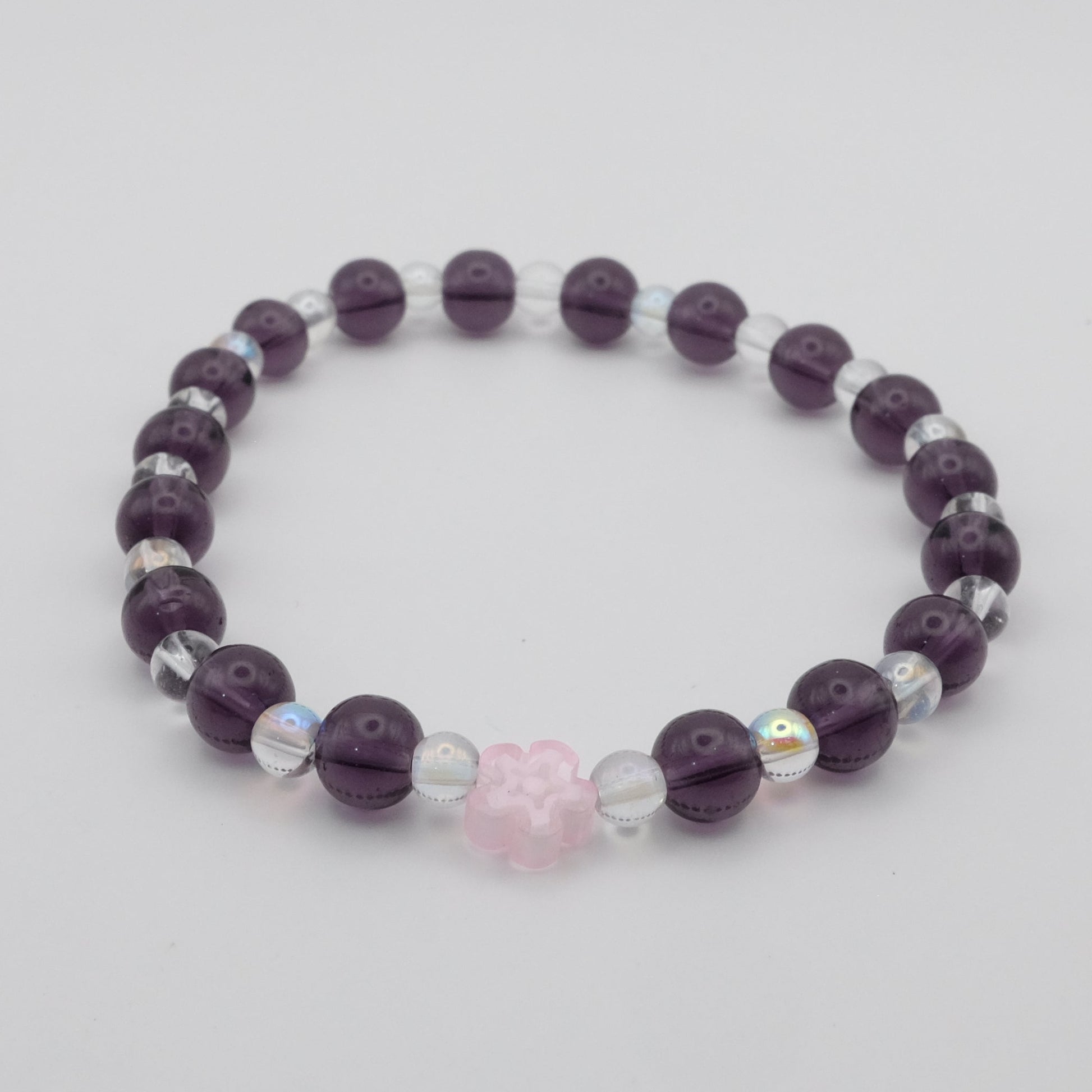 Purple beaded bracelet with a pink heart charm on a light gray background