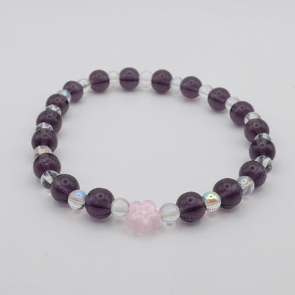 Purple beaded bracelet with a pink heart charm on a light gray background
