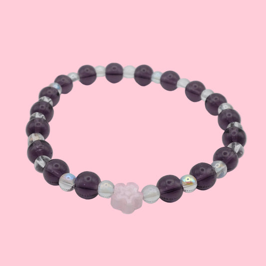 An elastic beaded bracelet composed of alternating 6mm deep purple glass beads and 4mm clear iridescent glass beads, featuring a soft pink glass flower bead at the centre, shown on a white background.