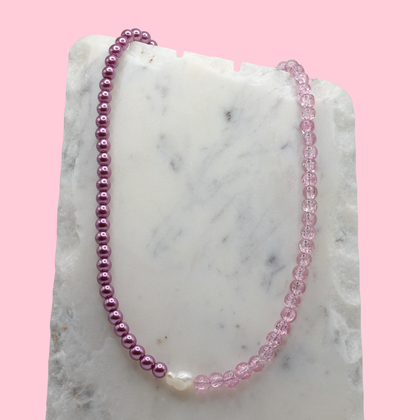 Necklace with pink and purple beads on a marble surface with a pink background